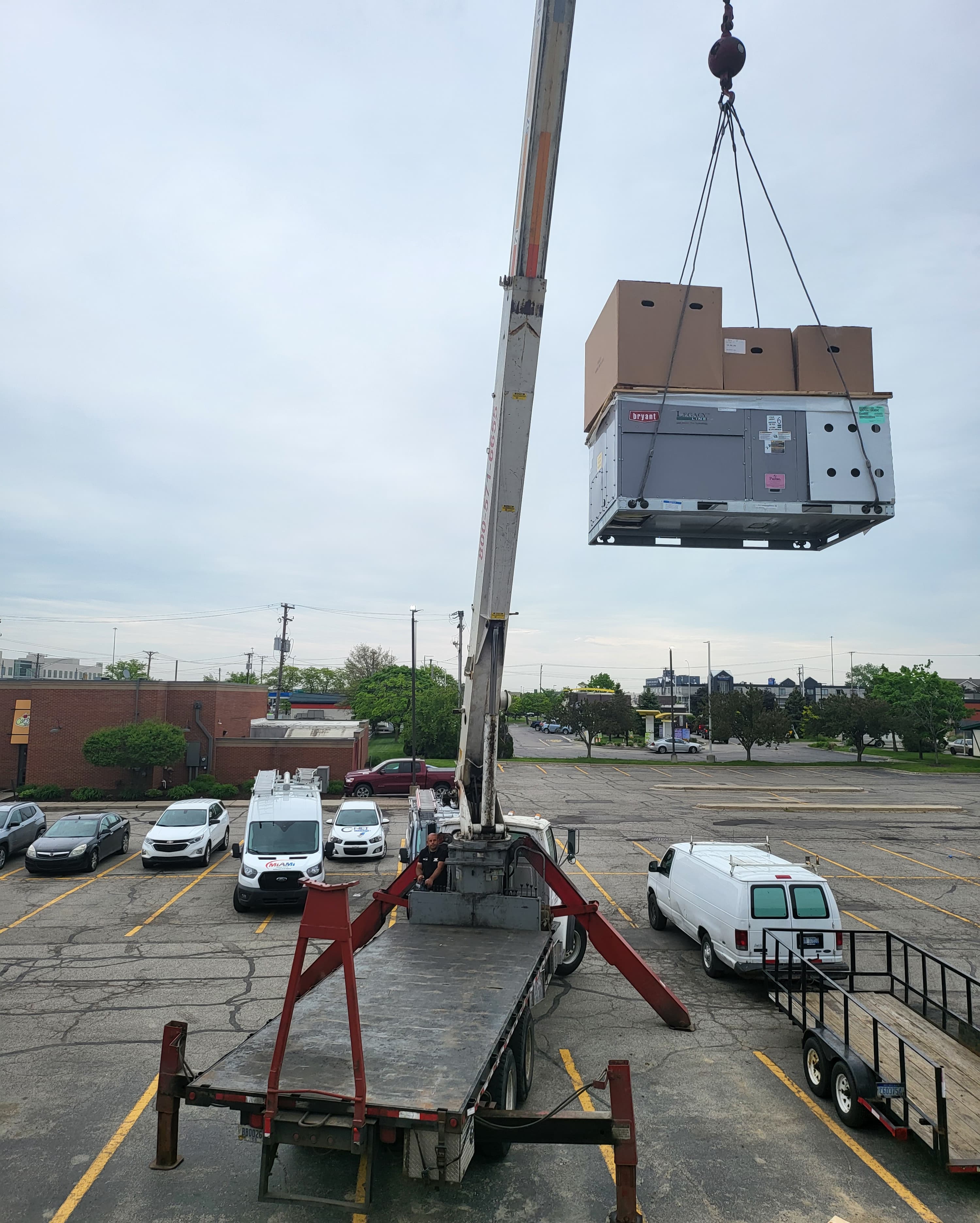 Crane operating while hoisting an HVAC unit above a rooftop installation area