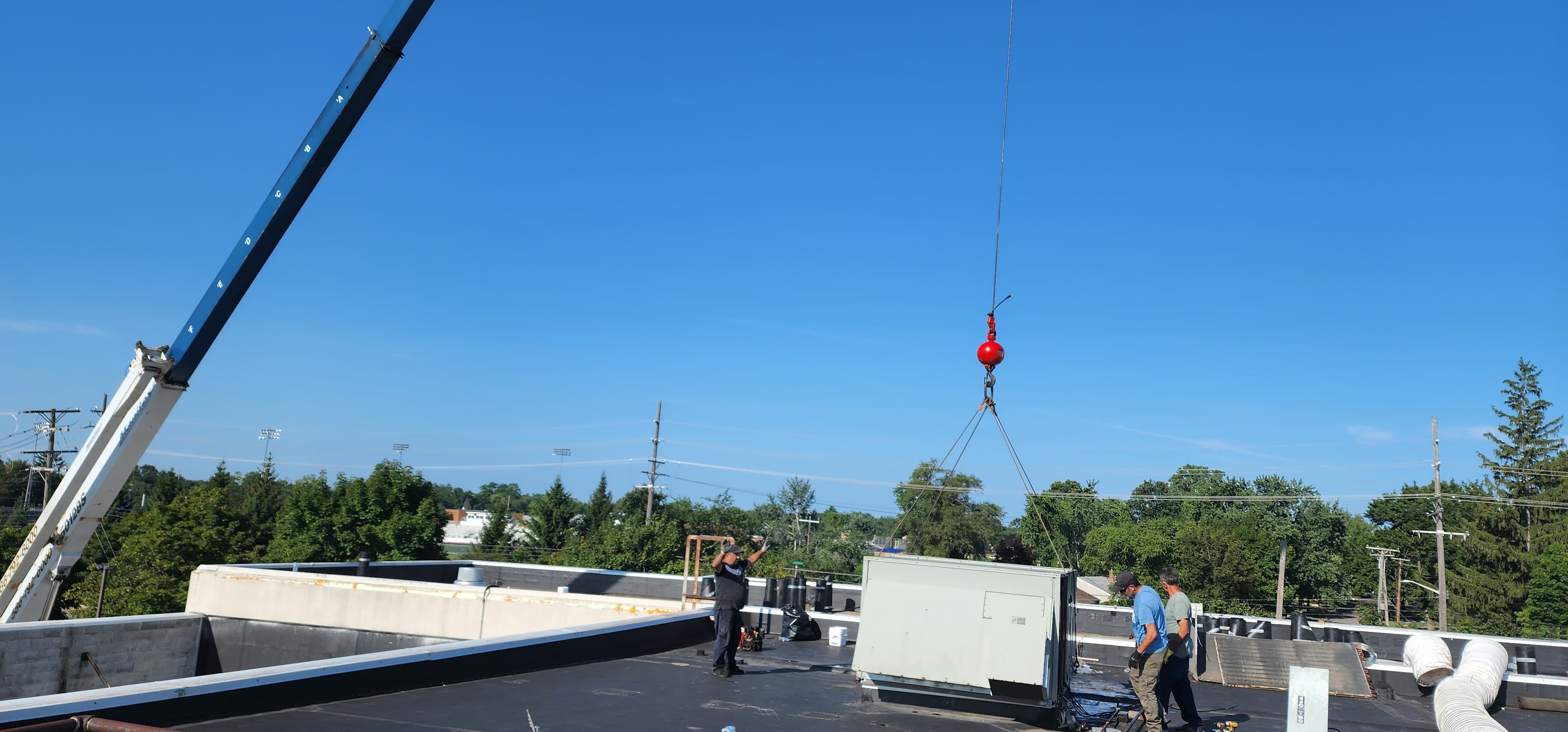 Technicians supervising rooftop unit placement during crane-assisted installation