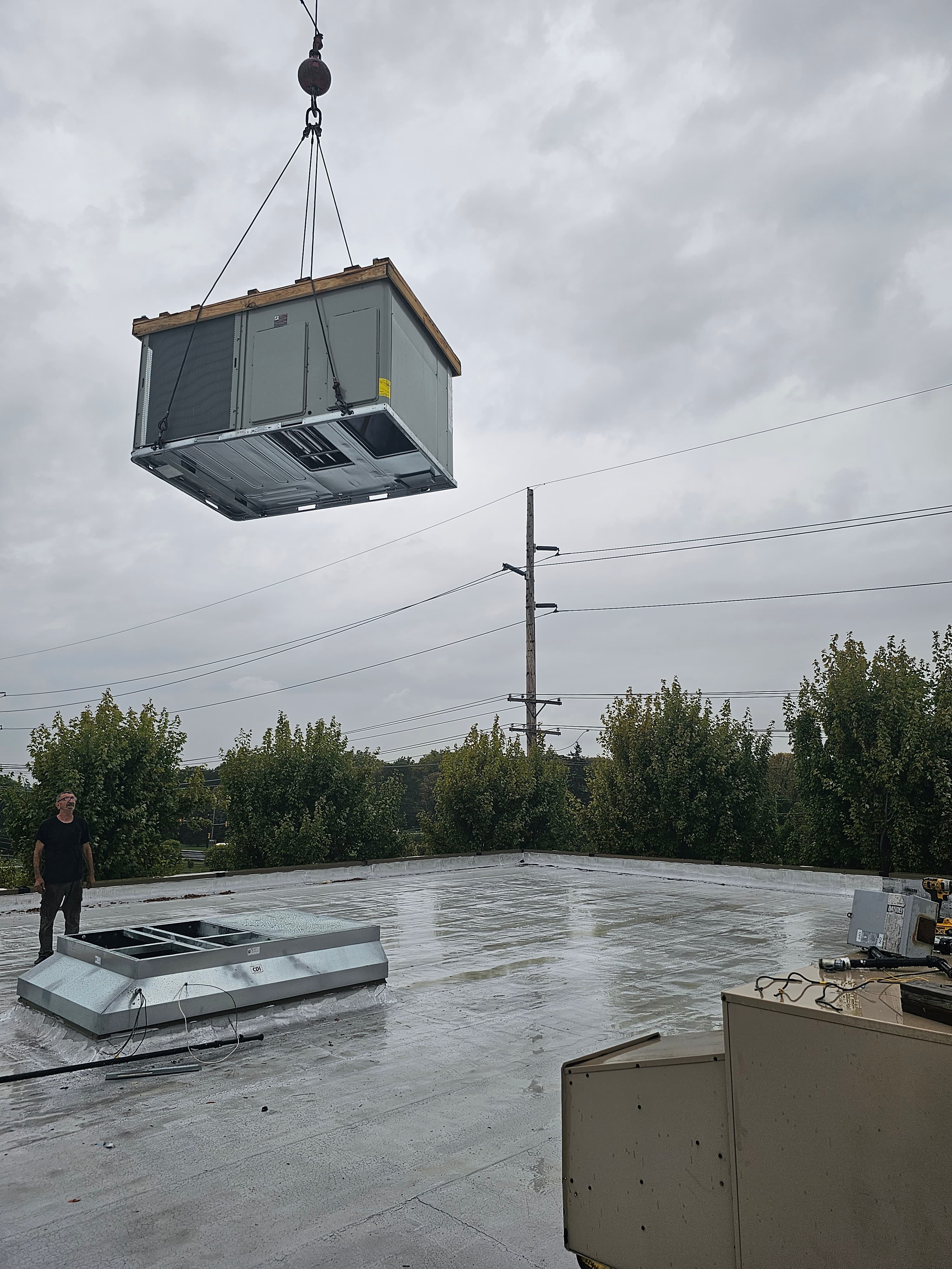 Crew supervising a hoisted HVAC unit before rooftop placement